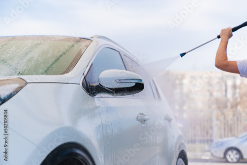 self-service car wash. a man in a work jumpsuit washes the car from a hose.  © andrey