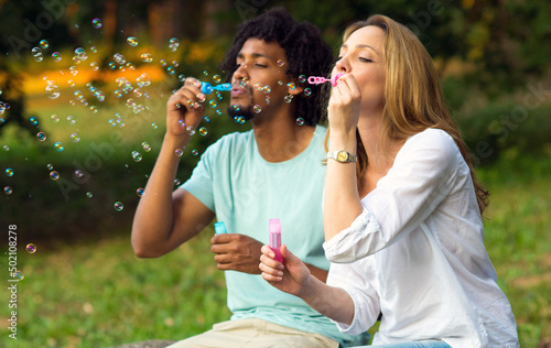 Young couple blowing soap bubbles while sitting in the summer nature