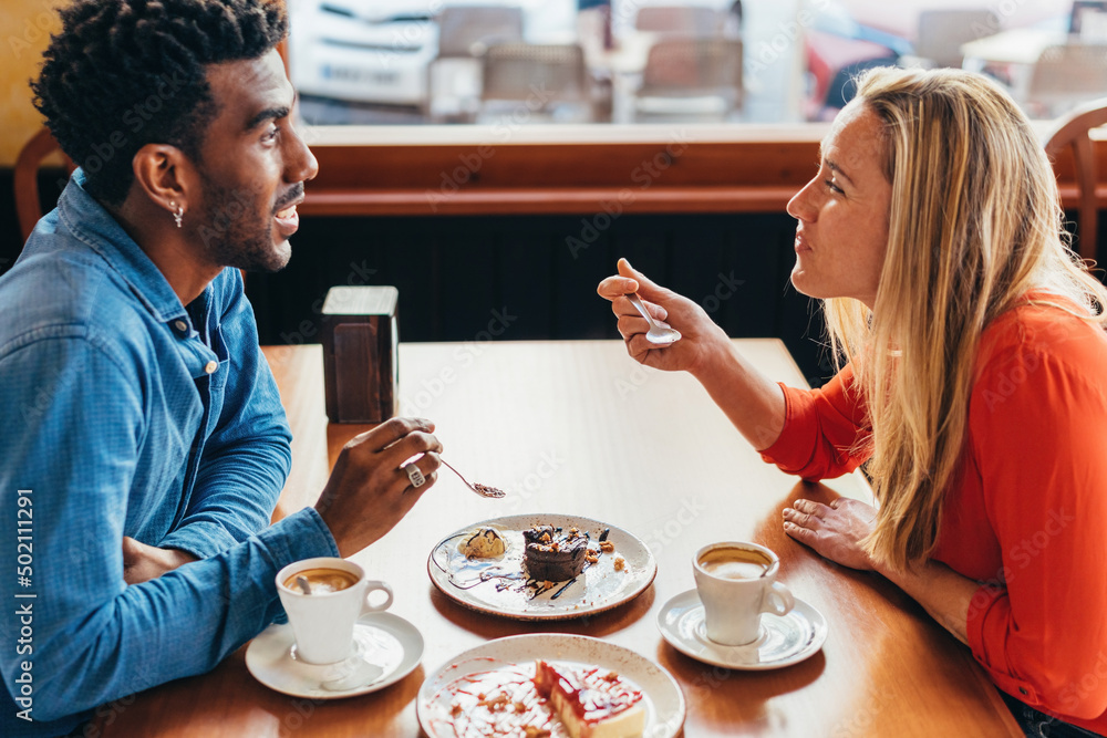 interracial couple having coffee and cake sitting at a table in a coffee shop