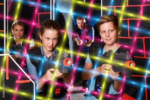 teen brother and sister with laser pistols playing laser tag in dark labyrinth with their parents