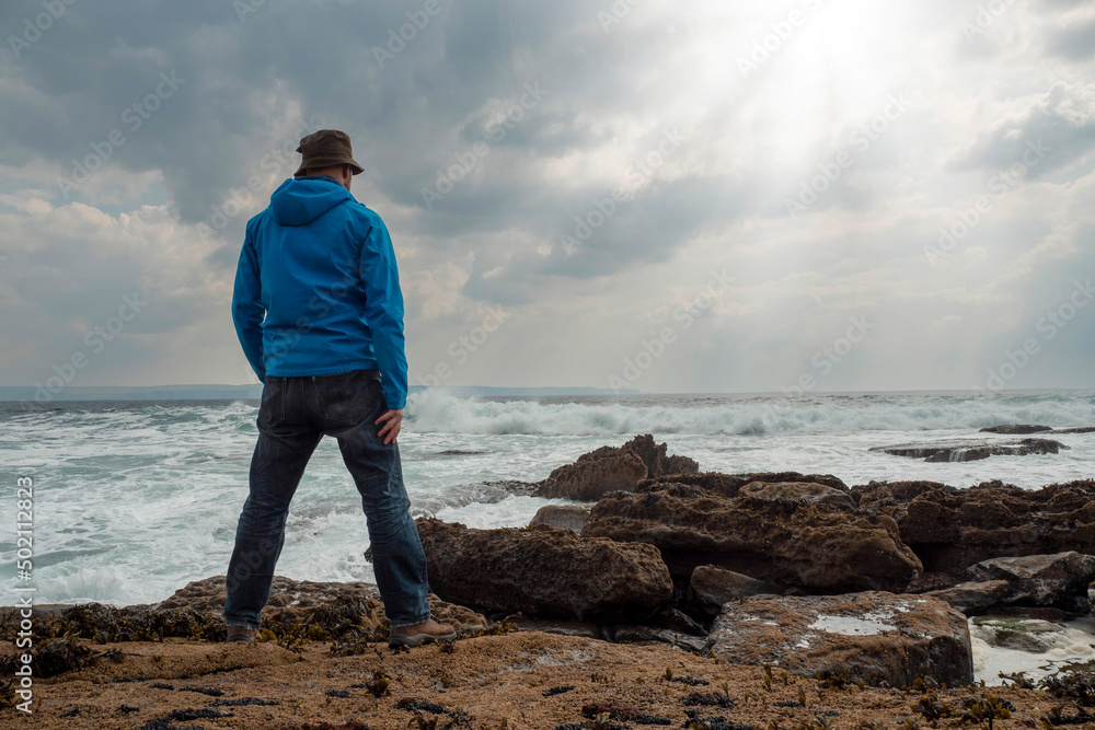 Male tourist standing on a rough stone coast. Aran island, county Galway, Ireland. Blue cloudy sky in the background. Travel and tourism concept. Beautiful Irish landscape in the background.