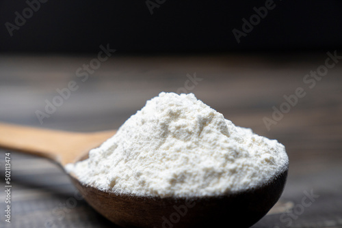 Whole flour in spoon on dark vintage wooden background. Close up view. Preparations for homemade baking. Basic ingredients for baking. Wheat flour on wooden spoon. 