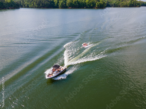 Wakeboard boat that is pulling a tube with people on it. Tubing on a wide open lake in summer time.