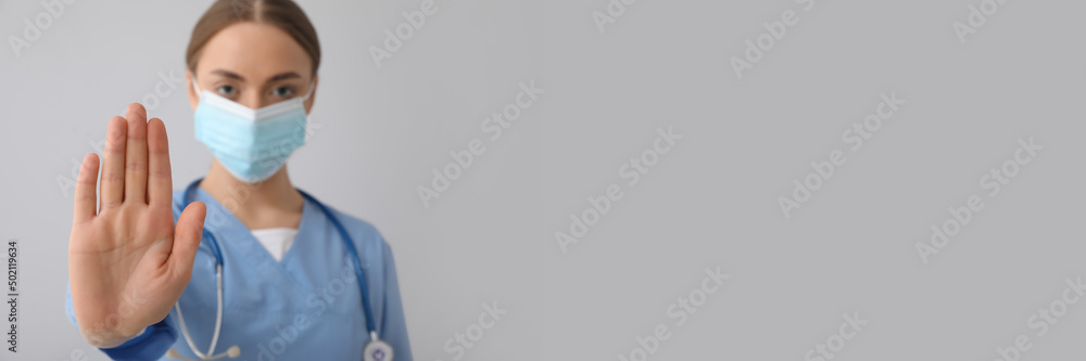 Female nurse in medical mask showing STOP gesture on grey background with space for text Female nurse in medical mask showing STOP gesture on grey background with space for text