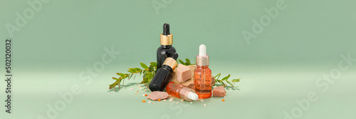 Bottles of cosmetic serum with herbal extract on green background with space for text