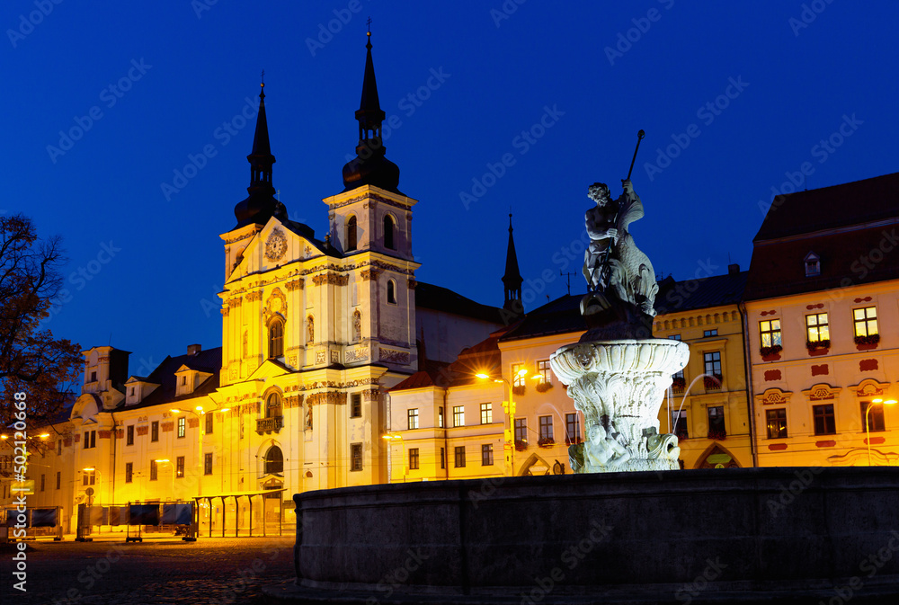 View of illuminated central square of Czech city of Jihlava overlooking medieval cathedral, steeple of Town Hall and Neptune Fountain at dusk