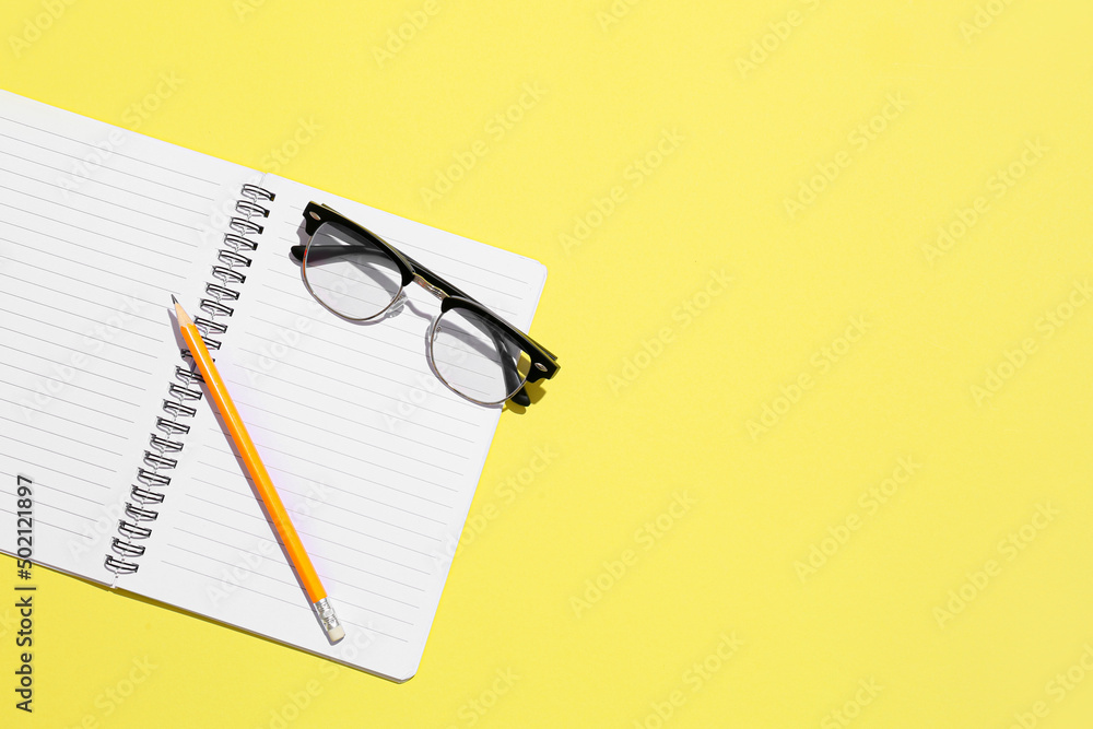 Stylish eyeglasses and notebook on yellow background Stylish eyeglasses and notebook on yellow background