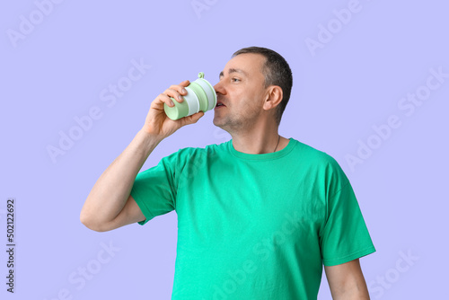 Mature man in green t-shirt drinking coffee on lilac background