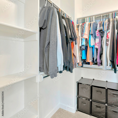 Square Small walk-in closet with hanging sweaters, shirts and blouse on the metal rods