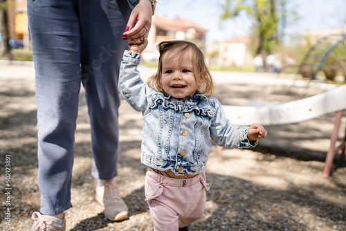 One baby small caucasian child little girl in park with her mother holding hand while play in bright spring day real people childhood development learning and family concept copy space happy smile