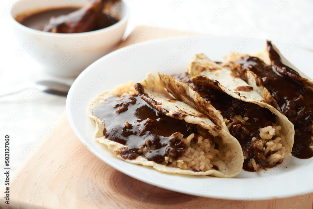 Tacos of mole with rice, placed on wood, in the background a piece of chicken Tacos of mole with rice, placed on wood, in the background a piece of chicken