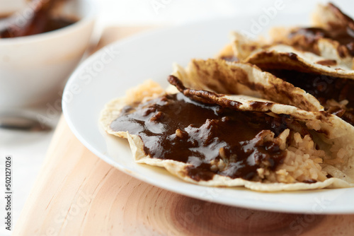 Tacos of mole with rice, placed on wood, in the background a piece of chicken