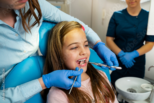 Little girl sitting in dentist chair  having routine checkup with a mirror  doctor doing checkup  nurse standing in the back 