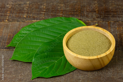 Mitragyna Speciosa Korth or kratom powder on wooden bowl wtih green leaf on rustic wooden background. 