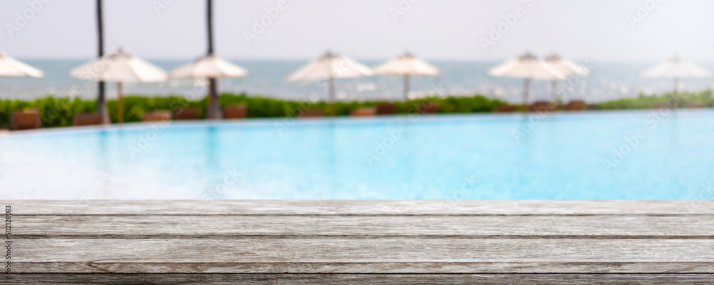 Empty wood table top and blurred swimming pool in tropical resort in summer banner background - can used for display or montage your products.