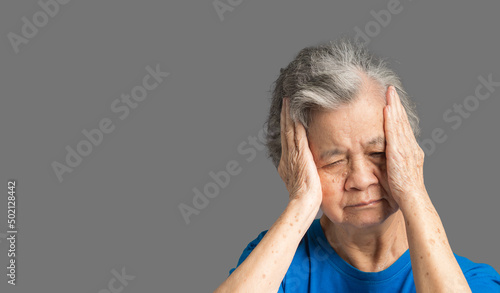 A senior woman who has a severe headache while standing on a blue background photo