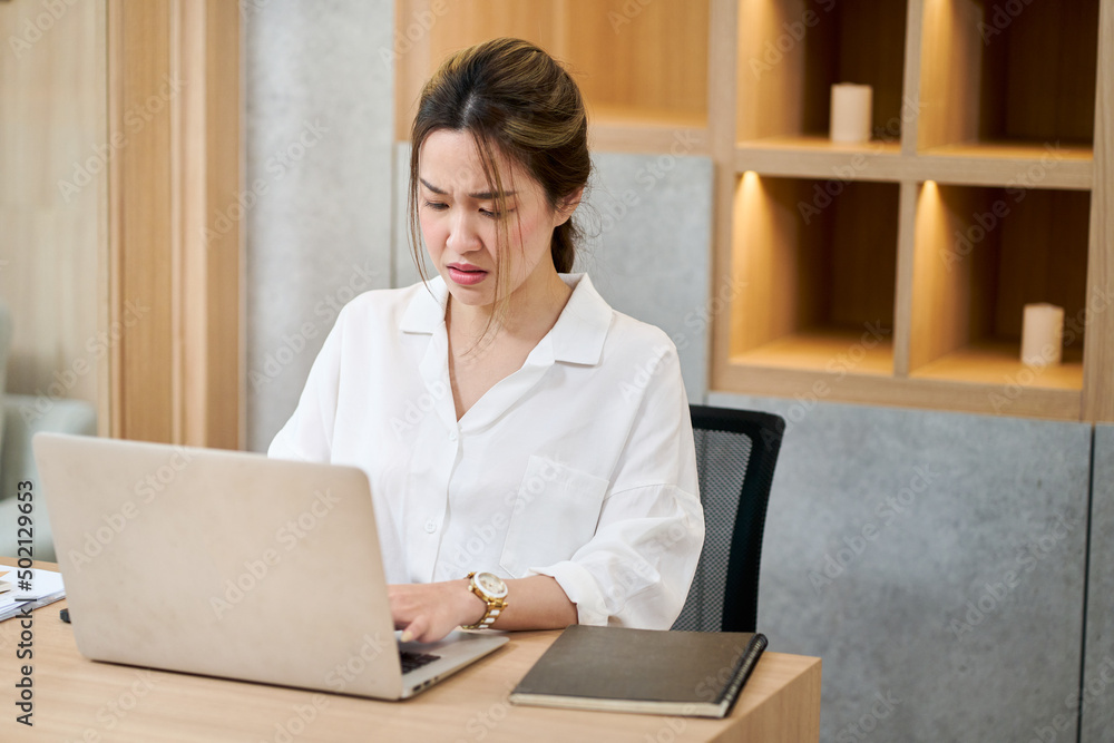 Asian working woman serious face looking to laptop in office Asian working woman serious face looking to laptop in office