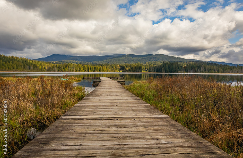 Idyllic view of a wooden pier in the lake with mountain scenery background in cloudy morning.