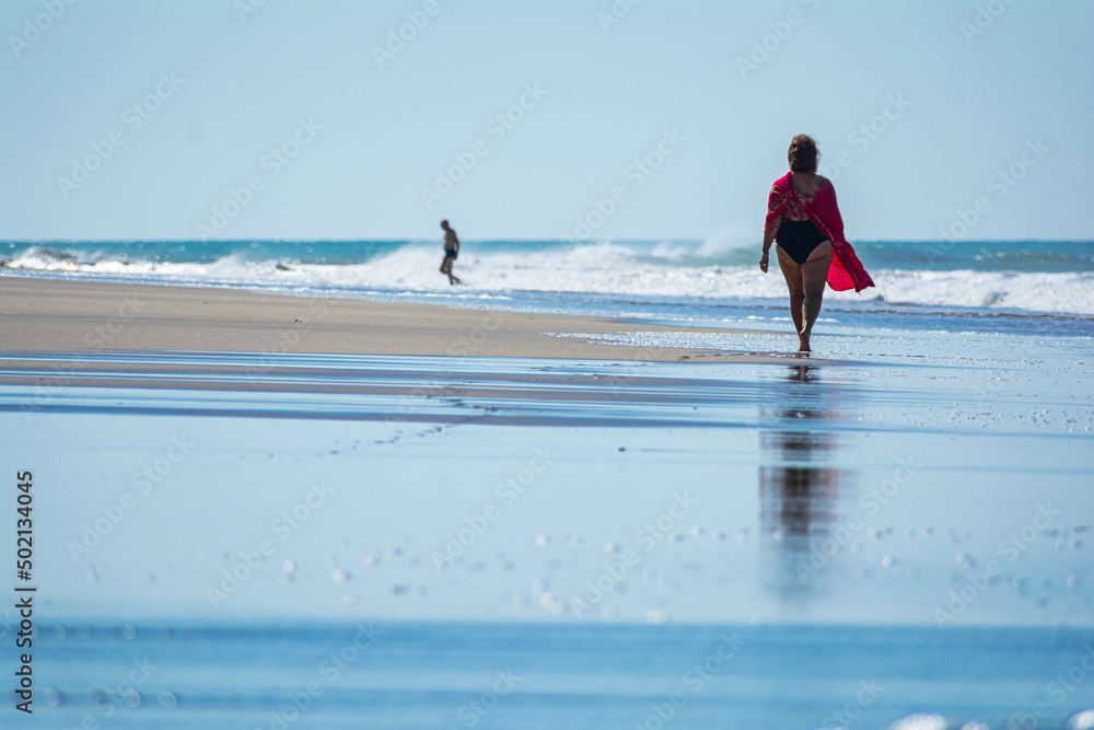 Caucasian woman walking along the seashore with a large dune in the background Caucasian woman walking along the seashore with a large dune in the background