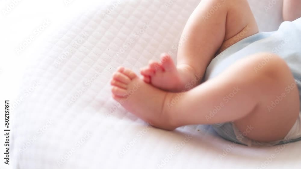 Cropped top view legs Newborn baby boy lying in nursery cocoon with blue clothes on bed in bedroom at home, Cropped top view legs Newborn baby boy lying in nursery cocoon with blue clothes on bed in bedroom at home,