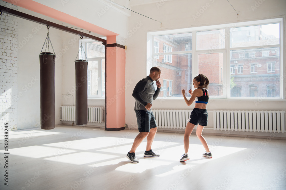 An attractive young boxer teaches his girlfriend boxing techniques in a loft equipped for boxing training