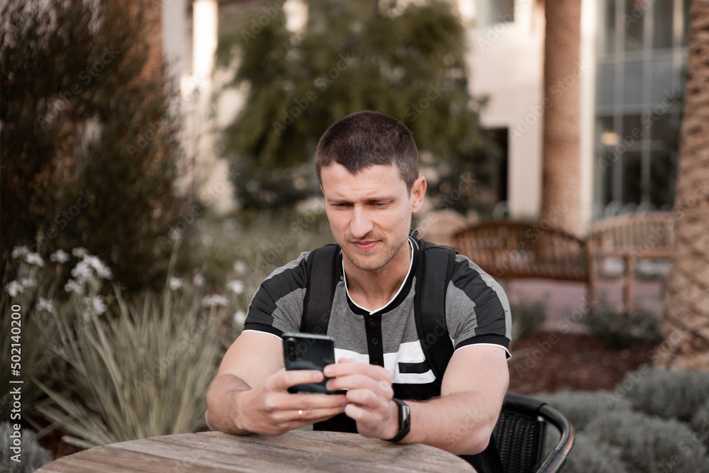 A young man or student or businessman sits at a table and looks into the phone. A young man or student or businessman sits at a table and looks into the phone.