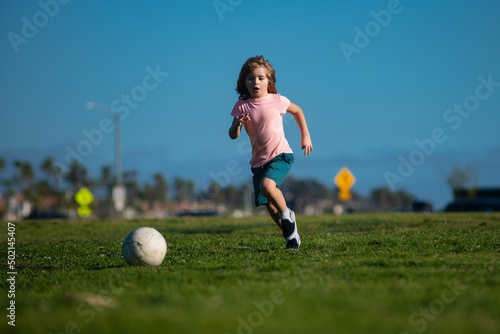 Excited child boy kicking ball in the grass outdoors. Soccer kids, children play football. © Volodymyr