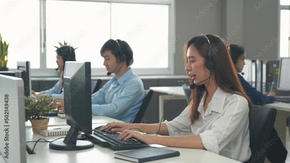 Call center young employee working with headset, Smiling customer support operator team at work surrounded by colleagues working in the office, Helpdesk customer services support agent concept Call center young employee working with headset, Smiling customer support operator team at work surrounded by colleagues working in the office, Helpdesk customer services support agent concept