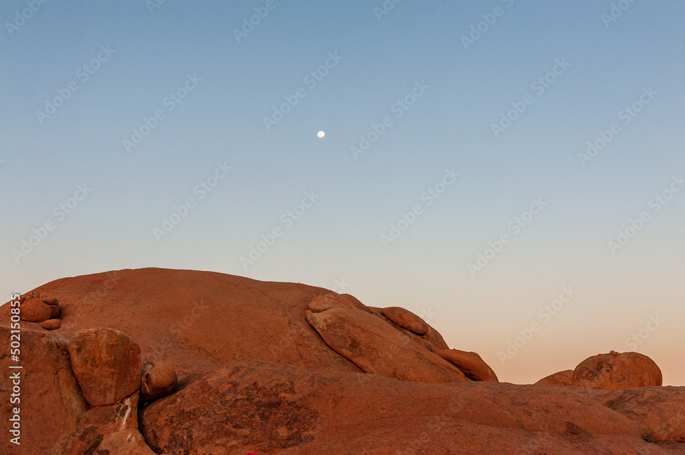 A bright moon over orange rocks. Sunset in the namibian desert, near Spitzkoppe.