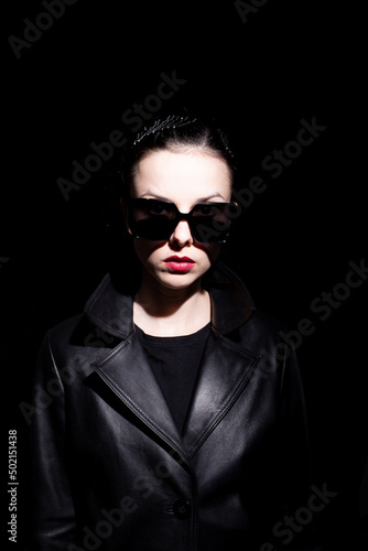 woman in leather coat and black sunglasses, black background