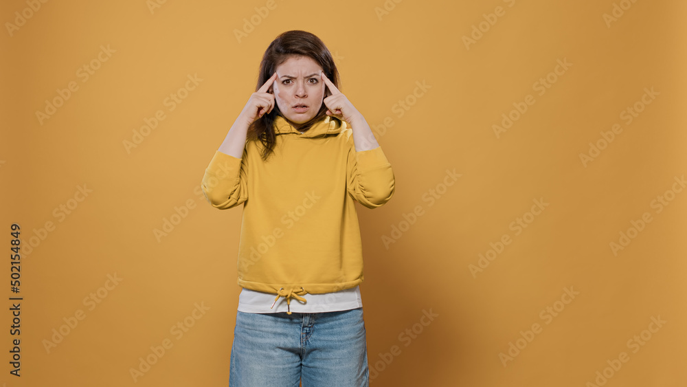 Focused woman thinking and concentrating having an idea touching temples with index fingers contemplating using imagination in studio. Casual young person wearing hoodie having inspiring thoughts. Focused woman thinking and concentrating having an idea touching temples with index fingers contemplating using imagination in studio. Casual young person wearing hoodie having inspiring thoughts.