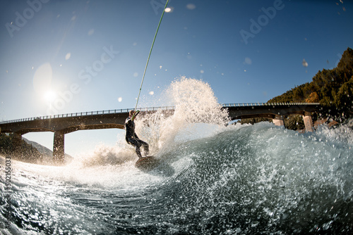 beautiful view on splashing river wave and man holding rope with handle and riding on wakesurf board © fesenko