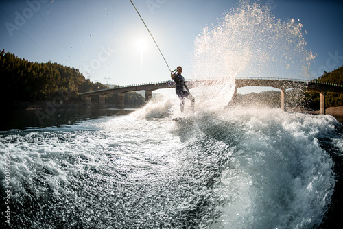 beautiful view on splashing river wave and guy holding rope with handle and riding on wakesurf board © fesenko