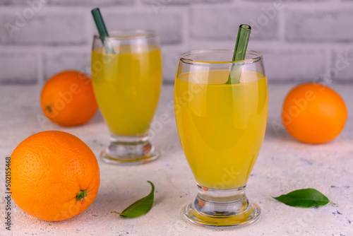 Orange juice in tall glasses and fresh oranges.