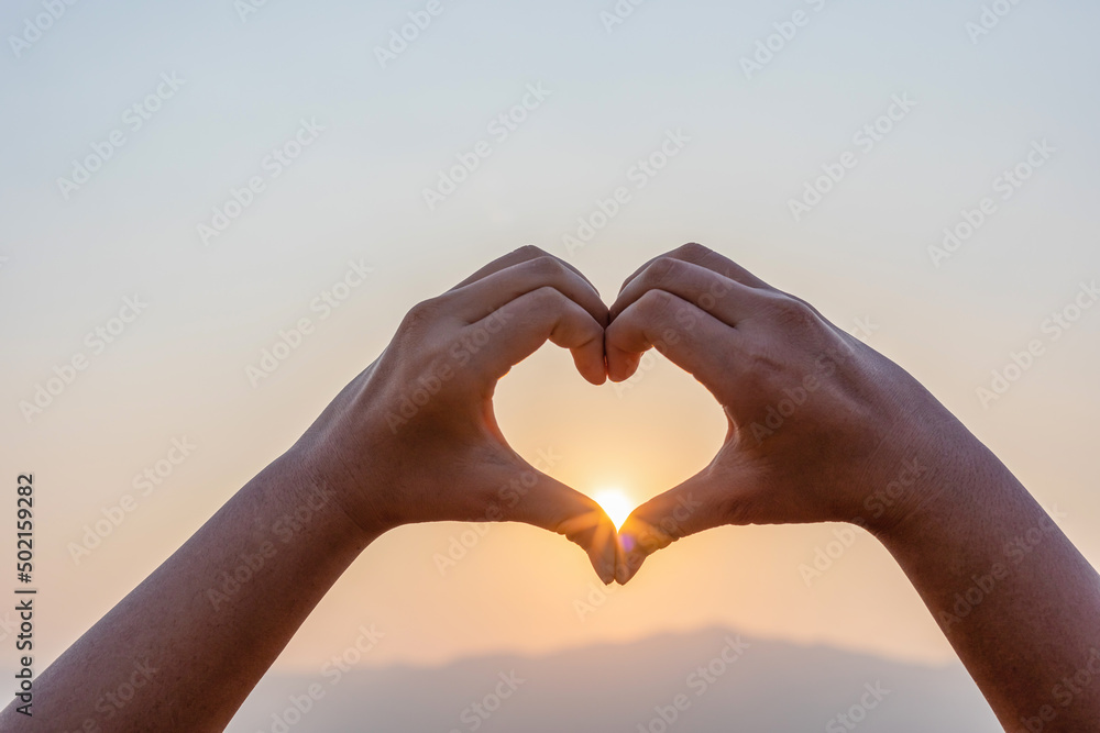Silhouette hands in heart shape on mountain outdoors in summer park at sunset Silhouette hands in heart shape on mountain outdoors in summer park at sunset