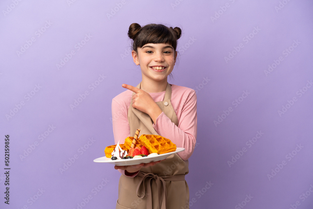 Little caucasian girl holding waffles isolated on purple background pointing to the side to present a product Little caucasian girl holding waffles isolated on purple background pointing to the side to present a product