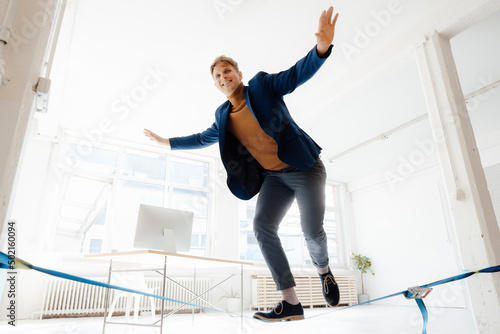 Happy businessman balancing on tightrope in office photo