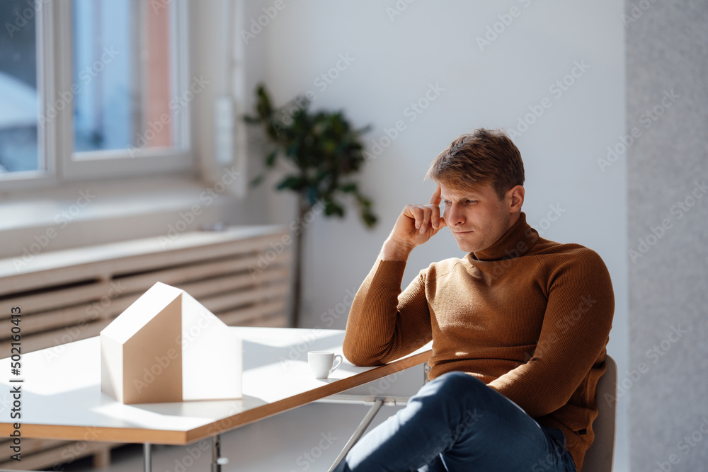 Thoughtful architect looking at model house in office Thoughtful architect looking at model house in office