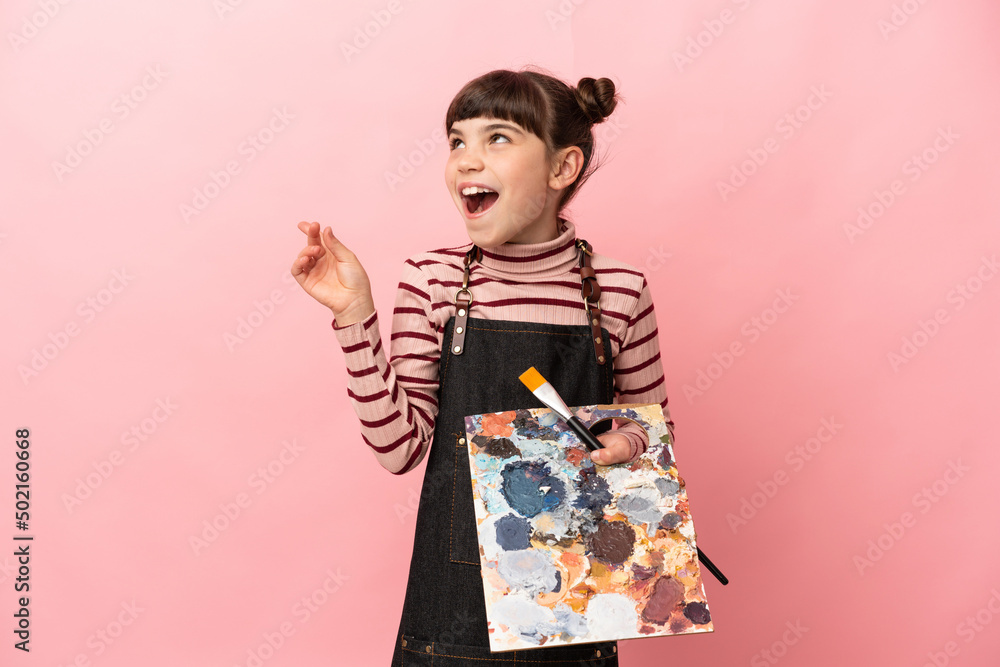 Little artist girl holding a palette isolated on pink background intending to realizes the solution while lifting a finger up Little artist girl holding a palette isolated on pink background intending to realizes the solution while lifting a finger up