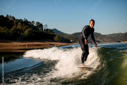 attractive man in wetsuit on wakesurf riding on splashing river wave