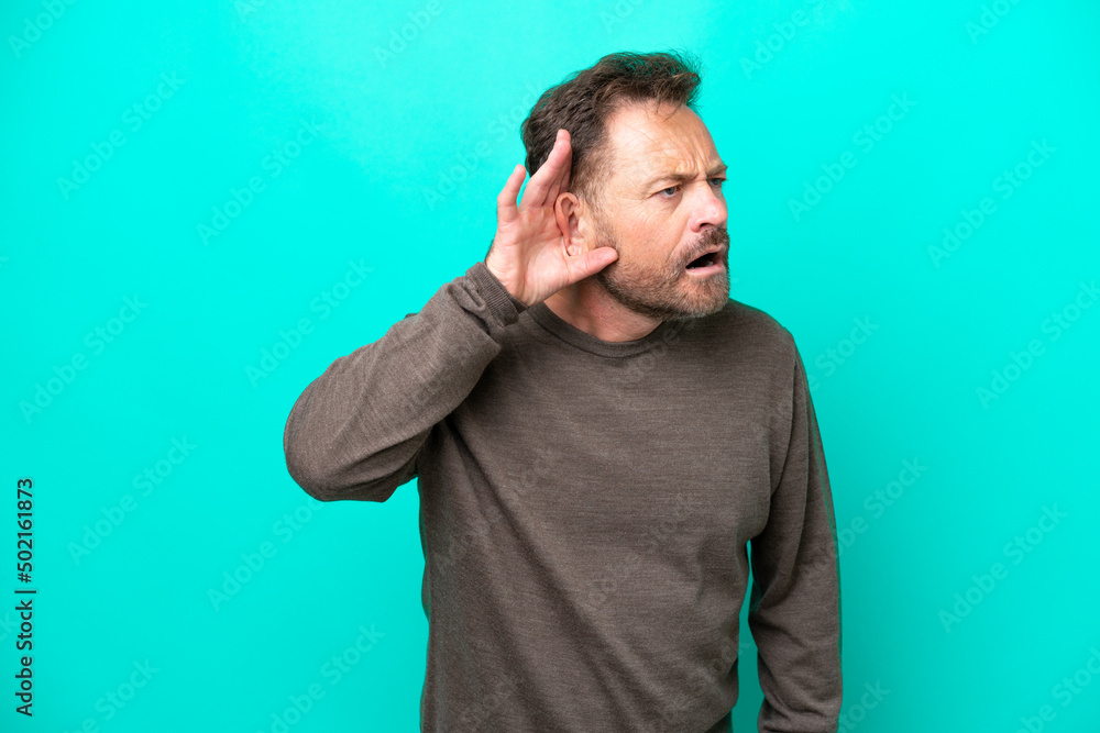 Middle age caucasian man isolated on blue background listening to something by putting hand on the ear Middle age caucasian man isolated on blue background listening to something by putting hand on the ear