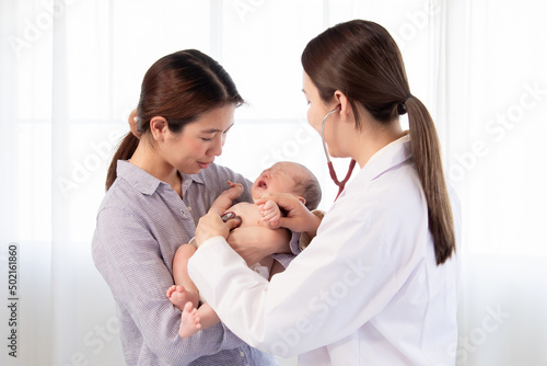 Asian woman doctor using stethoscope examining  on newborn baby in mother's arms. Mom holding adorable infant get sick crying in hospital. baby and health care concept.