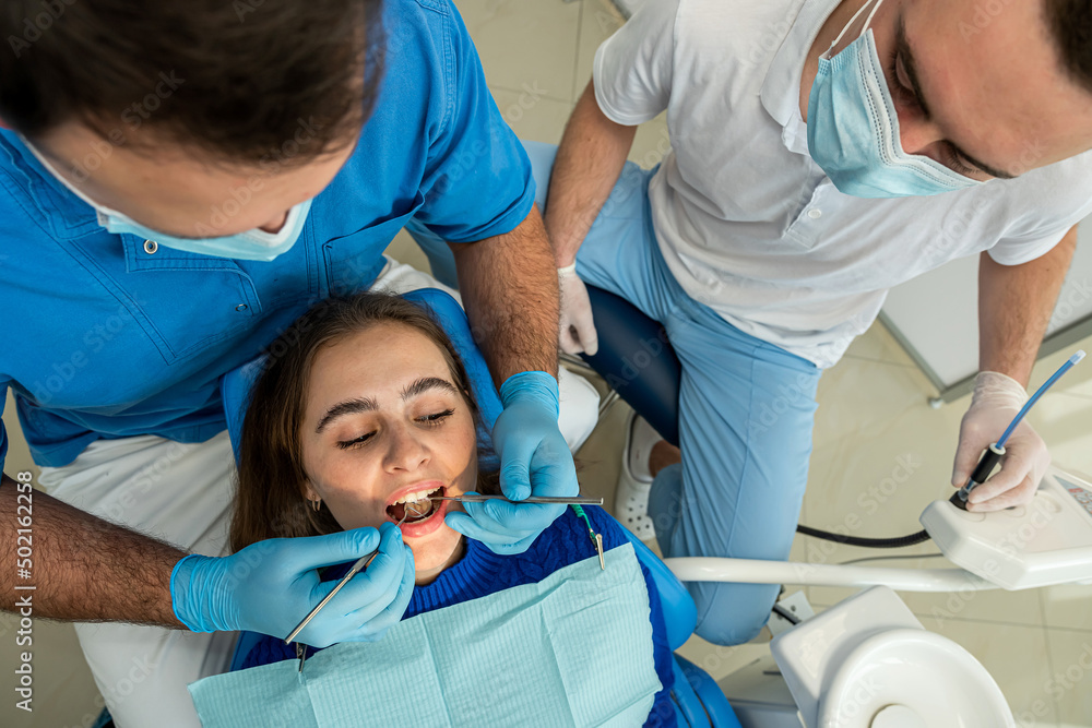 Pretty female patient sitting in armchair while doctor with assistant examining her teeth Pretty female patient sitting in armchair while doctor with assistant examining her teeth