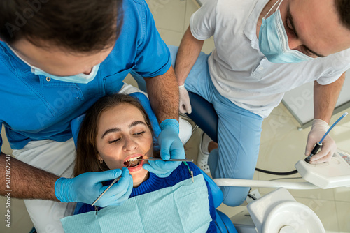 Pretty female patient sitting in armchair while doctor with assistant examining her teeth