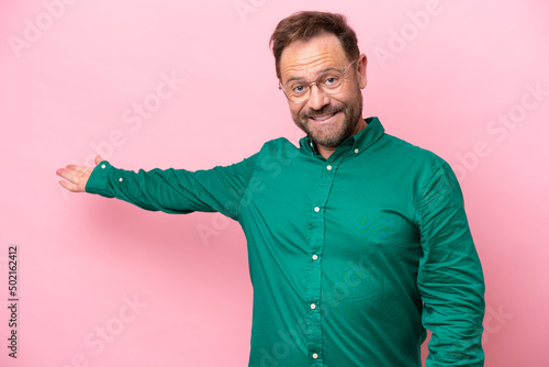Middle age caucasian man isolated on pink background extending hands to the side for inviting to come © luismolinero