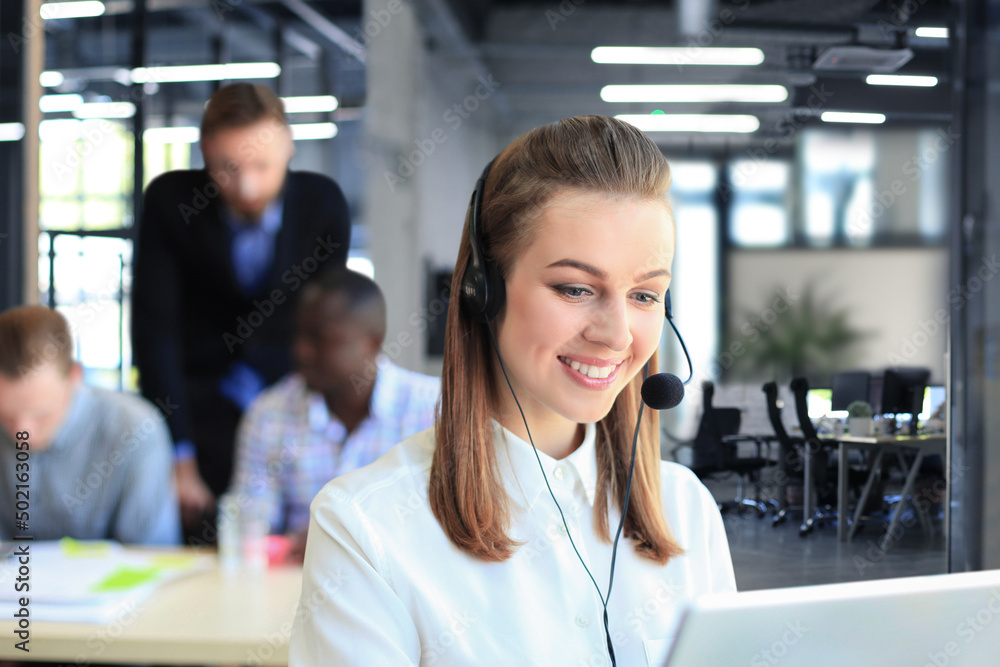 Fototapeta premium Portrait of call center worker accompanied by her team. Smiling customer support operator at work.