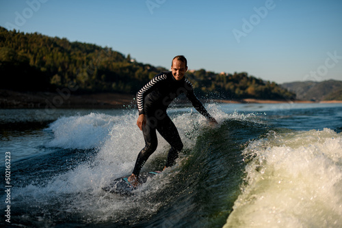 Cheerful man in wetsuit on wakesurf riding down the splashing wave