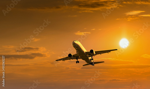 Passenger commercial aircraft flying under the clouds in sunset light.