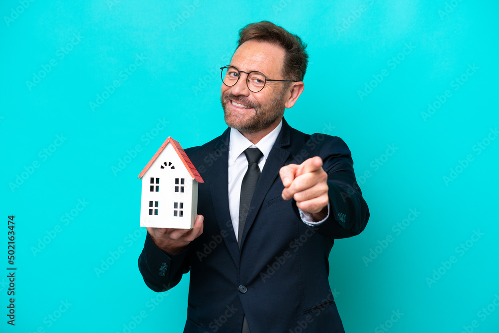 Real estate middle age agent man isolated on blue background pointing front with happy expression - obrazy, fototapety, plakaty 
