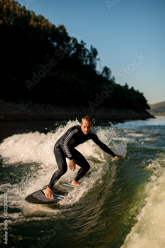 active man on wakesurf skilfully riding down the splashing wave